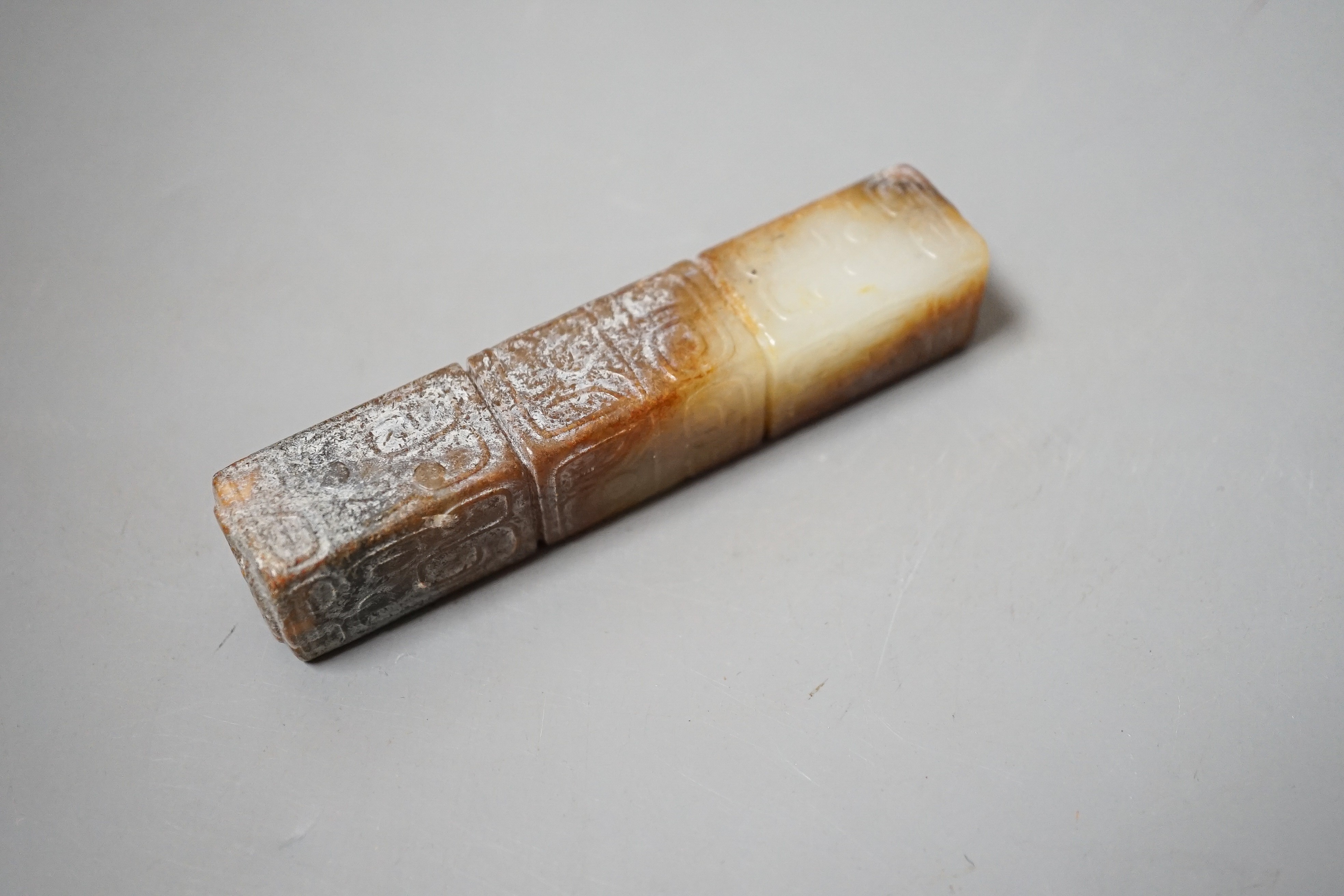 A Chinese archaistic white and russet jade handle mount, carved in relief with three registers of taotie masks, height 9.7cm